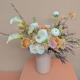 Arrangement of white calla lilies, roses, and peach flowers in a tall vase