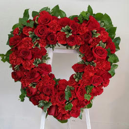 Heart-shaped wreath of red roses and carnations on a white stand