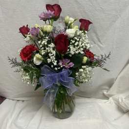 Mixed bouquet of red roses, white blooms, and purple flowers in a glass vase