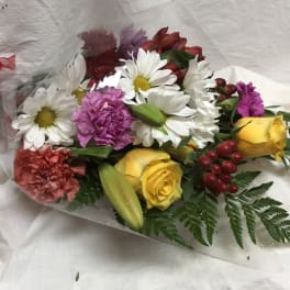 Mixed bouquet of daisies, roses, carnations, and lilies wrapped in clear plastic