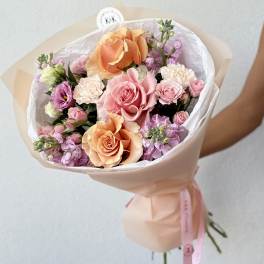 Bouquet of peach and pink roses with lavender blooms wrapped in pale paper