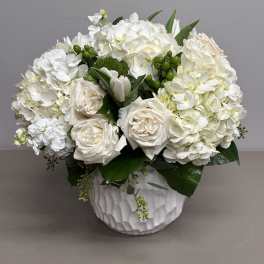 Low white arrangement of roses and hydrangeas in a textured white vase