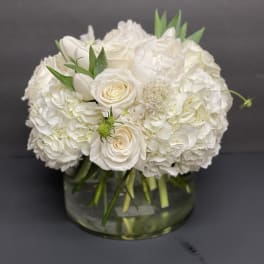 Low round arrangement of white roses, hydrangeas, and peonies in a clear glass vase