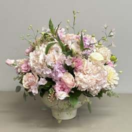 Low arrangement of blush and pink roses, hydrangeas, and mixed blooms in a white pedestal bowl