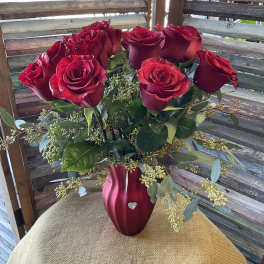 Red roses arranged in a red vase on a burlap-covered table