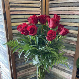 Red roses in a clear glass vase with fern foliage