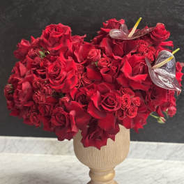 Red rose arrangement in a beige pedestal vase