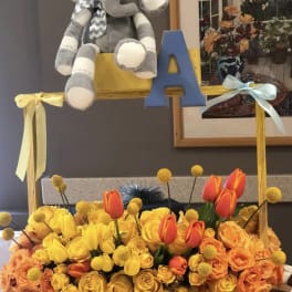 Yellow and orange flower arrangement with a plush elephant and blue letter A