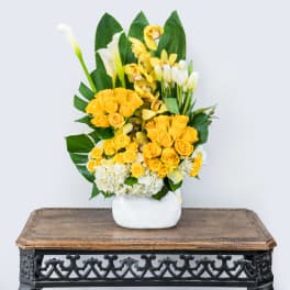 Yellow roses and white calla lilies arranged in a white vase