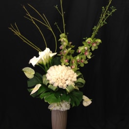 Tall floral arrangement with white roses, calla lilies, and green orchids in a vase