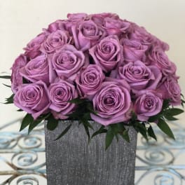 Lavender rose arrangement in a gray textured square vase on a decorative metal table