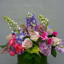 Mixed bouquet of roses, hydrangeas, and purple blooms in a glass vase