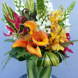 Tropical bouquet with orange calla lilies and yellow orchids in a glass vase