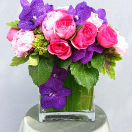 Pink roses and purple orchids arranged in a clear glass vase