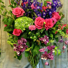 Tall bouquet of pink roses, purple flowers, and orchids in a glass vase