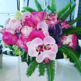 Pink and purple floral arrangement with orchids and roses in a white vase