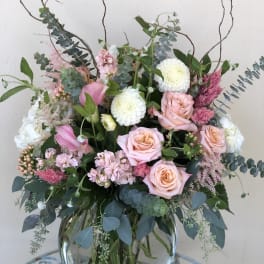 Tall pastel arrangement of pink roses, white mums, and calla lilies in a round glass vase