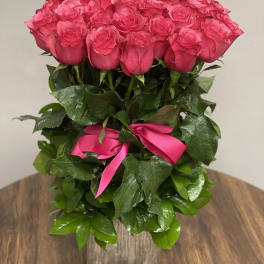 Tall arrangement of bright pink roses with a matching ribbon in a rustic wooden vase
