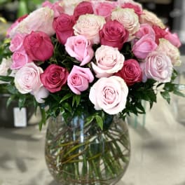 Large bouquet of pink roses in varying shades arranged in a round clear glass vase.