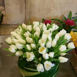 White tulips arranged in a round green glass vase