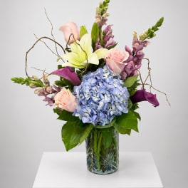 Mixed bouquet in a glass vase with blue hydrangea, pink roses, lilies, and purple blooms