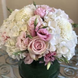 Low round arrangement of white hydrangeas, white dahlias, and pink roses in a green glass vase