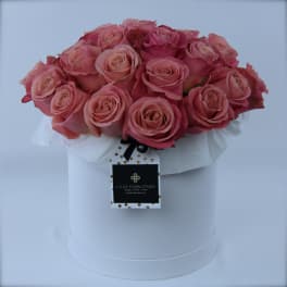 Pink roses arranged in a white hat box with a hanging tag
