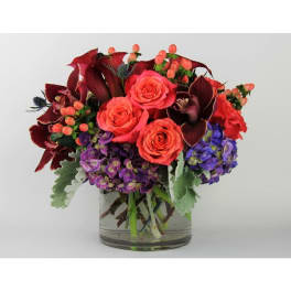 Bouquet of coral roses and purple flowers in a clear glass vase