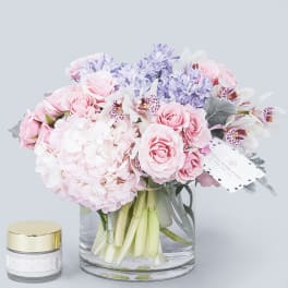 Pink and lavender bouquet in a clear glass vase with a small candle beside it