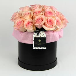 Pink roses arranged in a black hat box with a hanging tag