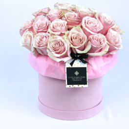 Pink roses arranged in a round hat box with a ribbon tag