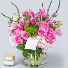 Pink tulips and roses arranged in a glass vase with a small candle beside it