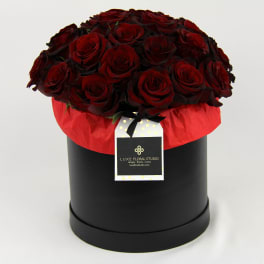 Red roses arranged in a black round box with a hanging tag