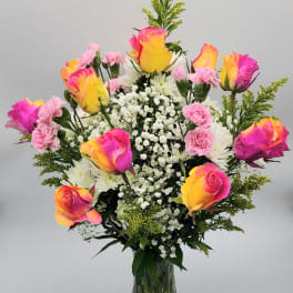 Bouquet of multicolored roses, white daisies, and pink carnations in a glass vase