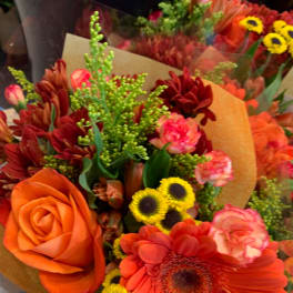 Bouquet of orange and red flowers with yellow accents wrapped in paper