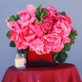 Pink rose and ranunculus arrangement in a square vase with a candle