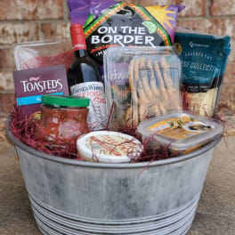 Gift basket with wine, crackers, chips, dip, and snacks in a metal tub