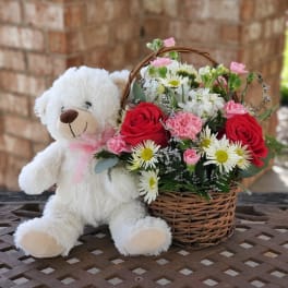 White teddy bear beside a basket of red and pink flowers