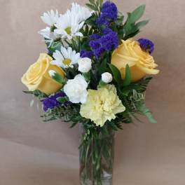 Bouquet of yellow roses, white daisies, and purple filler in a glass vase