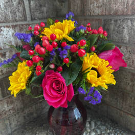 Bouquet of yellow sunflowers, pink roses, and red berries in a glass vase