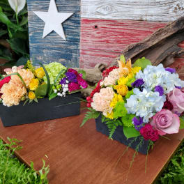 Two colorful floral arrangements in black boxes on a wooden table