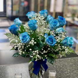 Blue roses in a glass vase with baby's breath and a blue ribbon