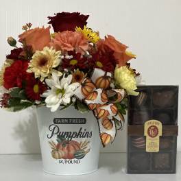 Fall flower arrangement in a pumpkin bucket beside a box of chocolates