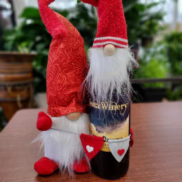 Two red gnome figurines stand beside a wine bottle on a table.
