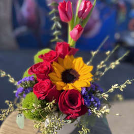 Bouquet of red roses, pink tulips, and a sunflower in a white vase