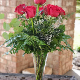 Tall vase arrangement of red roses with mixed greenery