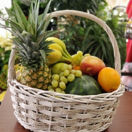 Wicker basket filled with assorted fruit including pineapple, bananas, grapes, and melon