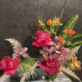 Pink roses and purple orchids arranged in a glass vase with orange accents