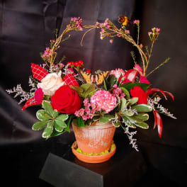 Mixed pink and red floral arrangement in a terracotta pot with a butterfly decoration