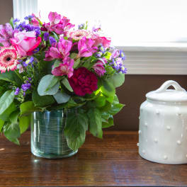 Pink and purple mixed bouquet in a glass vase beside a white ceramic jar